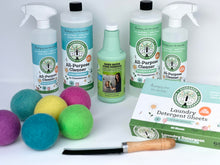 Load image into Gallery viewer, back row hows two large bottles of all-purpose cleaning solution with two spray bottles next to them, in the middle is a bottle of green hard water stain remover, on the left front is 6 multi-colored dryer balls, front right is a flat rectangular box of laundry detergent sheets and in the very front is a flat black brush with brown wooden handle
