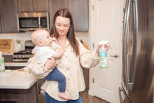Load image into Gallery viewer, women holding a baby in kitchen, spraying pur evergreen all purpose cleaner on a stainsteel fridge