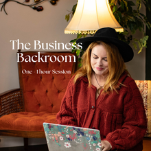 Load image into Gallery viewer, A woman wearing a black wide-brim hat and a textured rust-red button-up shirt sits in a cozy room, looking down at a laptop with a floral pattern. A warm orange tufted armchair, a glowing table lamp, and green foliage are visible in the background.