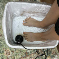Feet submerged in a foot bath with a black pump on a patterned floor.